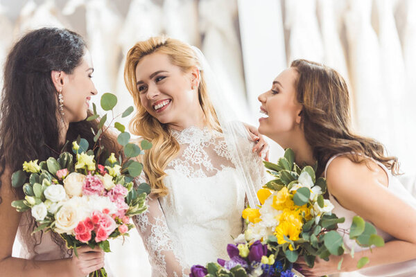 Bride in lace dress and bridesmaids with flowers in wedding fashion shop