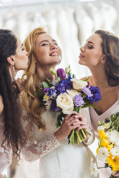 Happy women in wedding dresses with flowers in wedding atelier