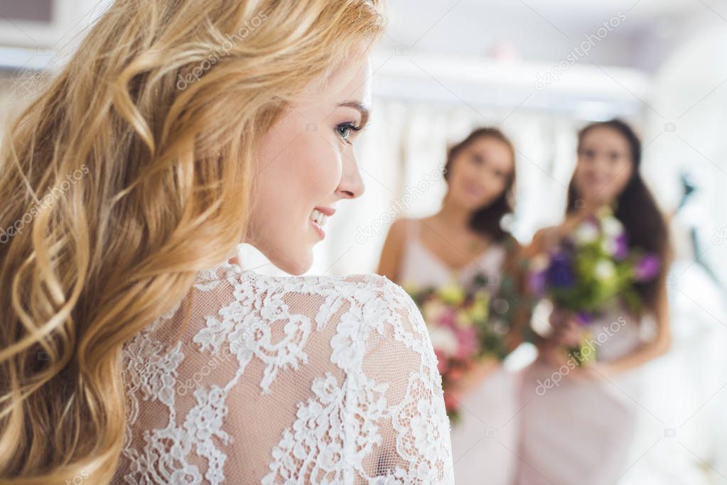 Bride in lace dress and bridesmaids with flowers in wedding fashion shop
