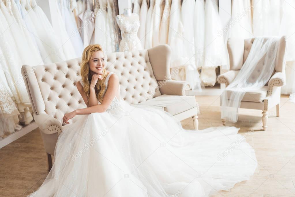 Young bride in tulle dress sitting on sofa in wedding salon