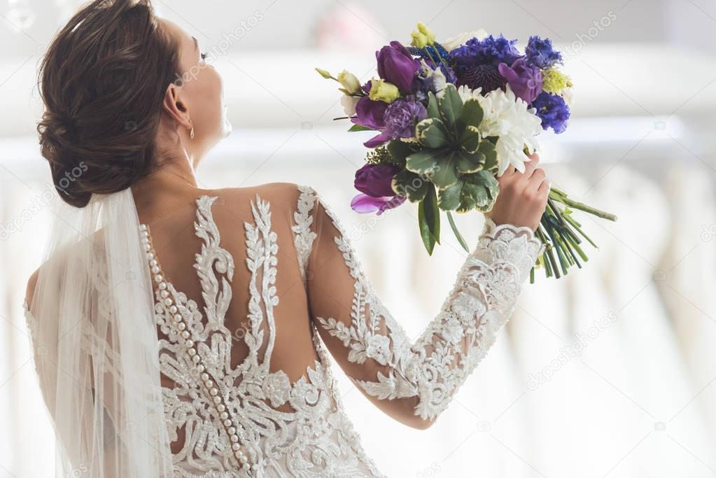 Rear view of bride in lace dress with flowers in wedding fashion shop