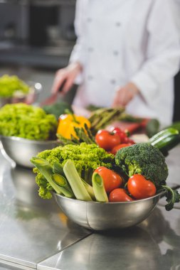 cropped image of chef cooking at restaurant kitchen with vegetables on foreground clipart
