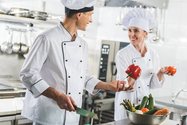 smiling chef giving red bell pepper to colleague at restaurant kitchen