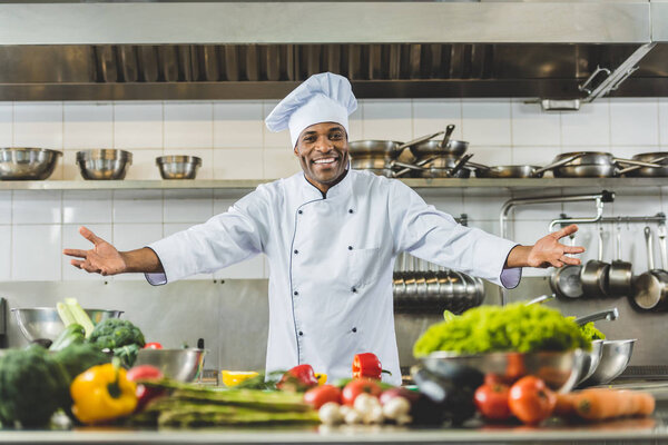 handsome african american chef standing with open arms at restaurant kitchen