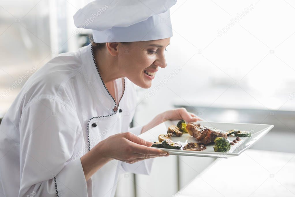 attractive chef sniffing cooked steak at restaurant kitchen