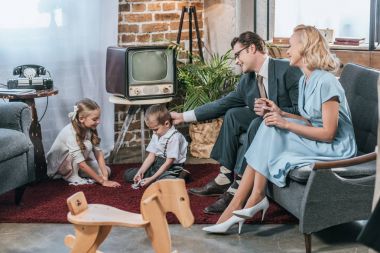 kanepede oturan ve 1950'ler tarzı evde, domino taşlarla oynayan küçük çocuklar bakarak mutlu anne