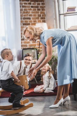 mutlu anne, baba ve kardeş 50s evde, sallanan at üzerinde oturan sevimli küçük çocuk bakarak stili