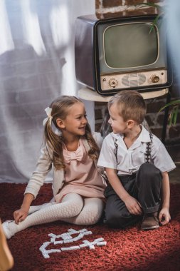 happy little children in 1950s style clothes playing with domino tiles at home clipart