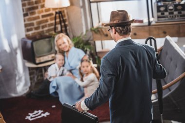 selective focus of mother with two kids playing together and looking at father coming home, 1950s style clipart