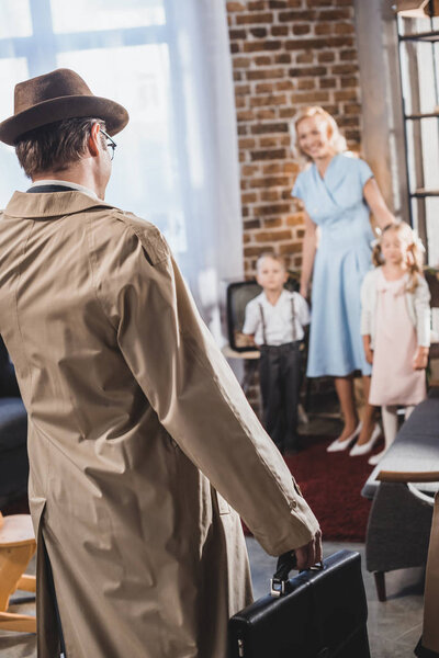 back view of father with briefcase coming home and looking at happy family, 1950s style