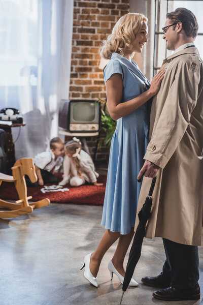 Счастливые старомодные мужчина и женщина улыбаются друг другу свистят милые маленькие дети, играющие позади
