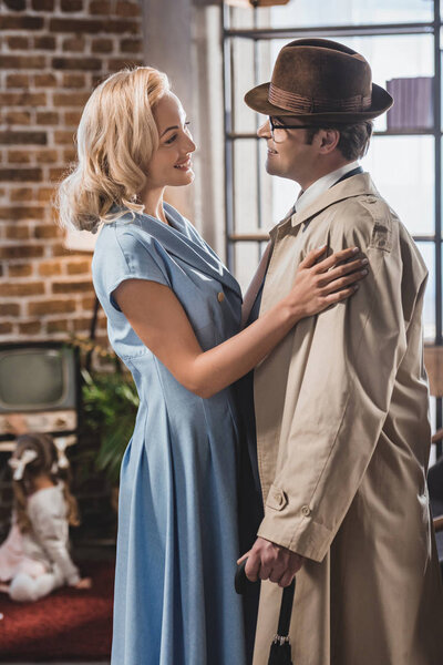 вид сбоку счастливой женщины, смотрящей на улыбающегося мужа, возвращающегося домой, в стиле 1950-х годов
