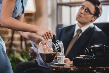 cropped shot of woman pouring coffee to husband in suit reading newspaper, 1950s style clipart