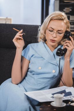 Sigara ve vintage telefonla konuşurken gözlük güzel sarışın kadın