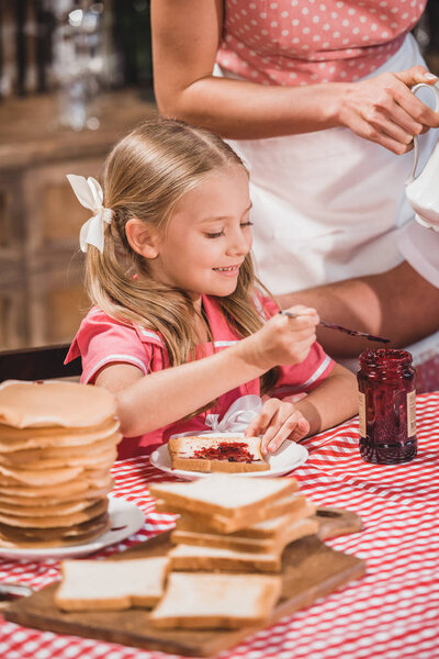 cute smiling little girl eating delicious toast with jam for breakfast