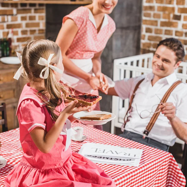 拍摄的微笑的父母看着可爱的女儿吃烤面包果酱早餐 二十世纪五十年代风格的家庭 — 图库照片