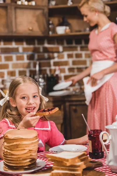 Adorable Niña Comiendo Tostadas Con Mermelada Sonriendo Cámara Mientras Madre —  Fotos de Stock