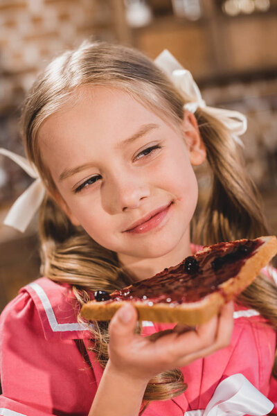 adorable happy little girl eating toast with jam