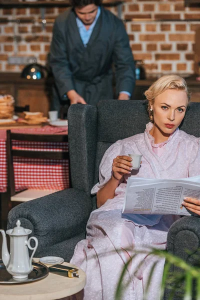 Mujer Bata Sosteniendo Periódico Taza Café Mientras Marido Prepara Desayuno —  Fotos de Stock