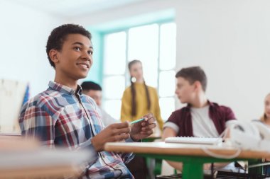 Düşük açılı görünümü arkasında oturan sınıf arkadaşları ve Afro-Amerikan lise öğrencisi elinde kalem tutan