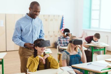 Standing teacher and multicultural high school teenage students using virtual reality headsets  clipart