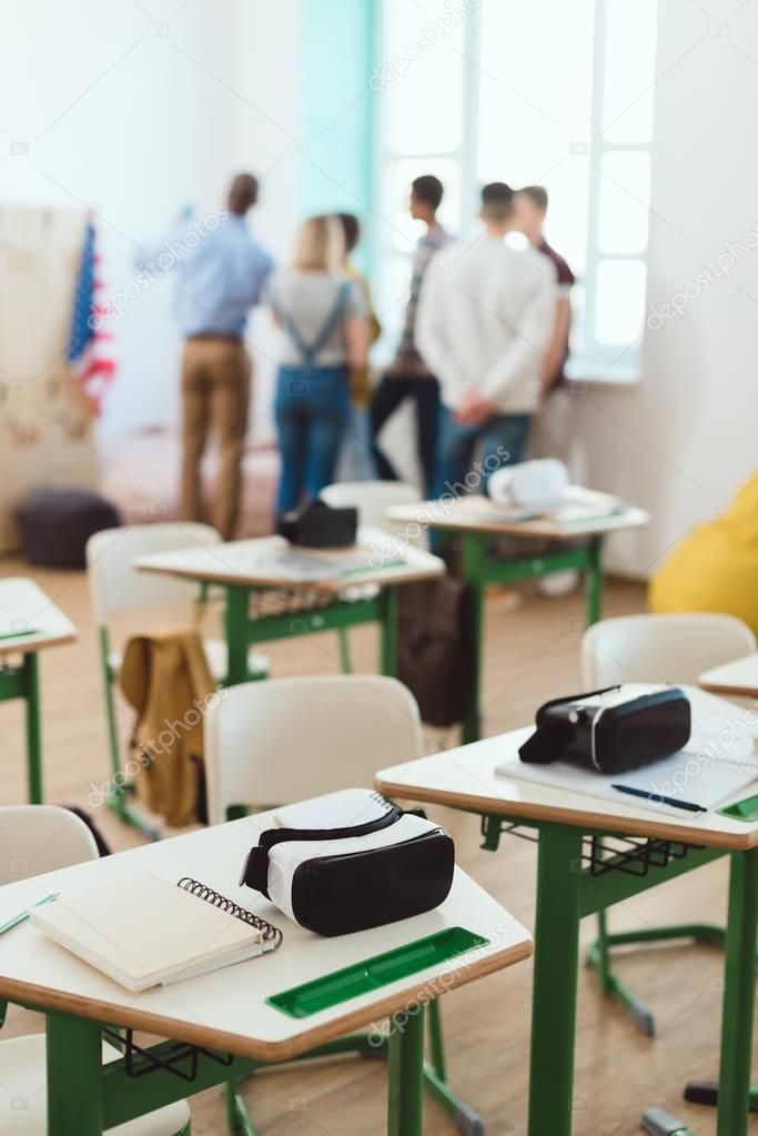 Virtual reality headsets on tables and teacher with schoolchildren standing behind