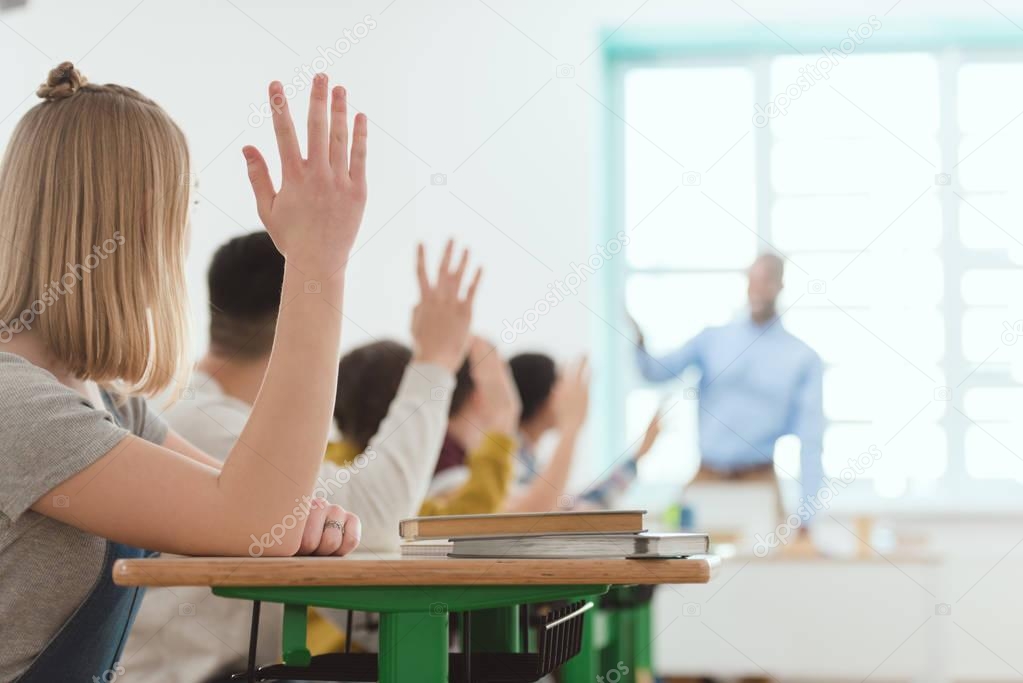 high school students raising hands to answer teachers question