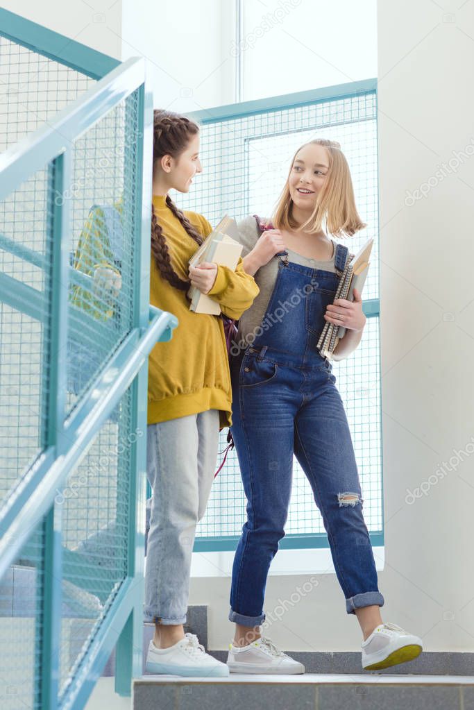 teenage schoolgirls with backpacks and books walking on stairs
