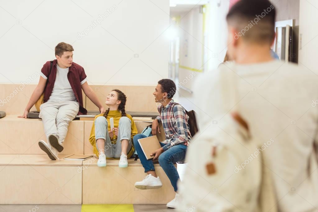 group of high school students sitting at school corridor and chatting