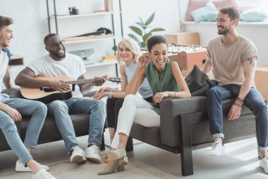 bir grup insan eğleniyor ve gitar çalmak çok ırklı gülümseyen genç 