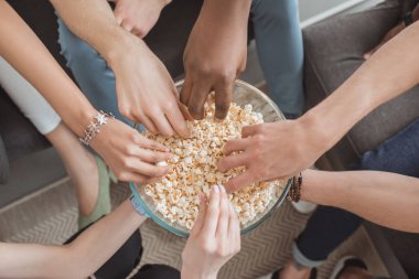 top view of female and male hands taking popcorn from bowl 
