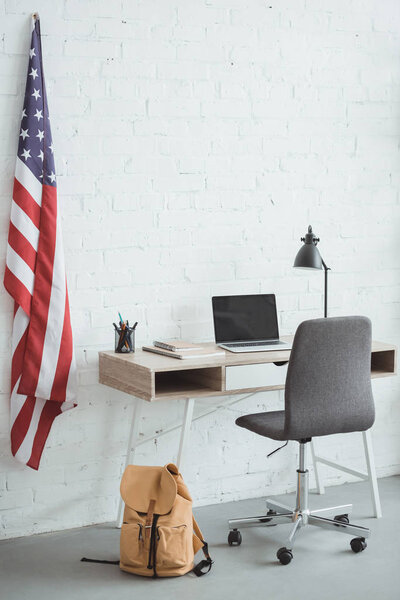 интерьер современной гостиной с американским флагом на кирпичной стене и столом с ноутбуком
