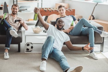 üç çok kültürlü gençler salon futbol maçı izlerken ve bira şişeleri ile kutluyor 