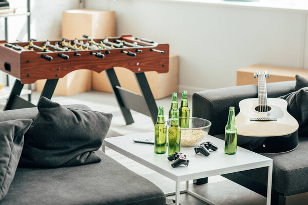 интерьер современной гостиной с настольным футболом, пивными бутылками, джойстиками и гитарой
 