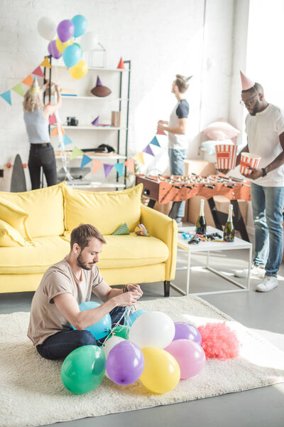 group of multicultural friends decorating room with party garlands and balloons 