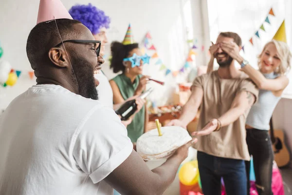 Happy Friends Covering Eyes Young Man Greeting Him Birthday Cake — Stock Photo, Image