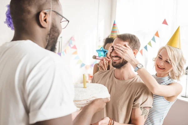 Happy Friends Covering Eyes Young Man Greeting Him Birthday Cake — Stock Photo, Image