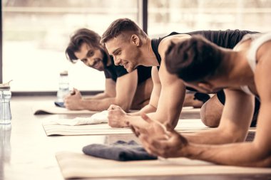 side view of smiling handsome sportsmen talking and simultaneously doing plank in gym clipart