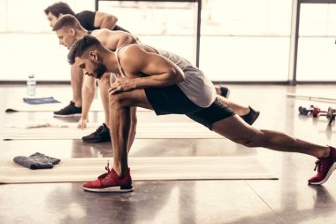 handsome sportsmen simultaneously stretching legs in gym clipart