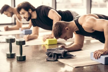handsome sportsmen simultaneously doing plank and using blocks in gym clipart