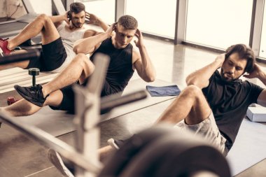 handsome sportive friends doing sit ups together in gym clipart