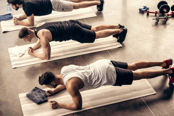 high angle view of muscular sportsmen simultaneously doing plank in gym