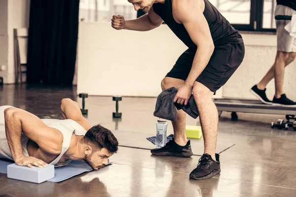 Pelatih Mendukung Olahragawan Melakukan Papan Pada Blok Yoga Gym — Stok Foto