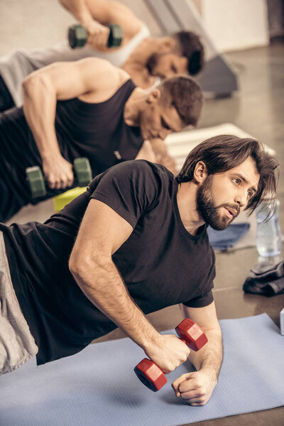 handsome sportsmen simultaneously training with dumbbells on floor in gym