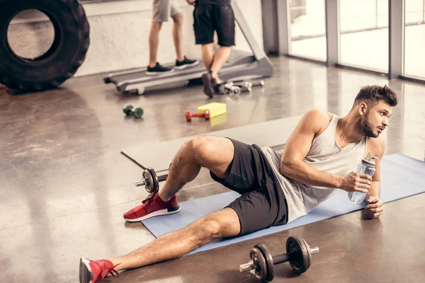 英俊的运动员躺在地板上的健身房和捧瓶水 — 免费的图库照片