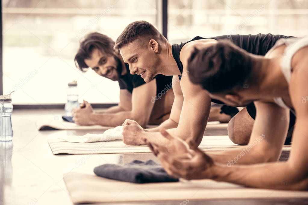 side view of smiling handsome sportsmen talking and simultaneously doing plank in gym