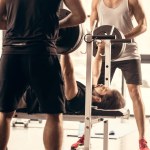 运动员帮助朋友锻炼杠铃在体操台上的压力
