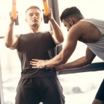 Trainer hilft jungen Sportlern beim Training mit Aufhängebändern im Fitnessstudio