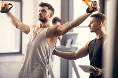 Dijital tablet direnç şeritli spor salonunda egzersiz sporcu bakarak ile genç eğitmeni