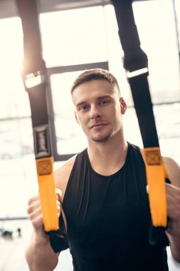 Fitness kayışları ile eğitim ve spor salonunda kamera bakarak yakışıklı delikanlı